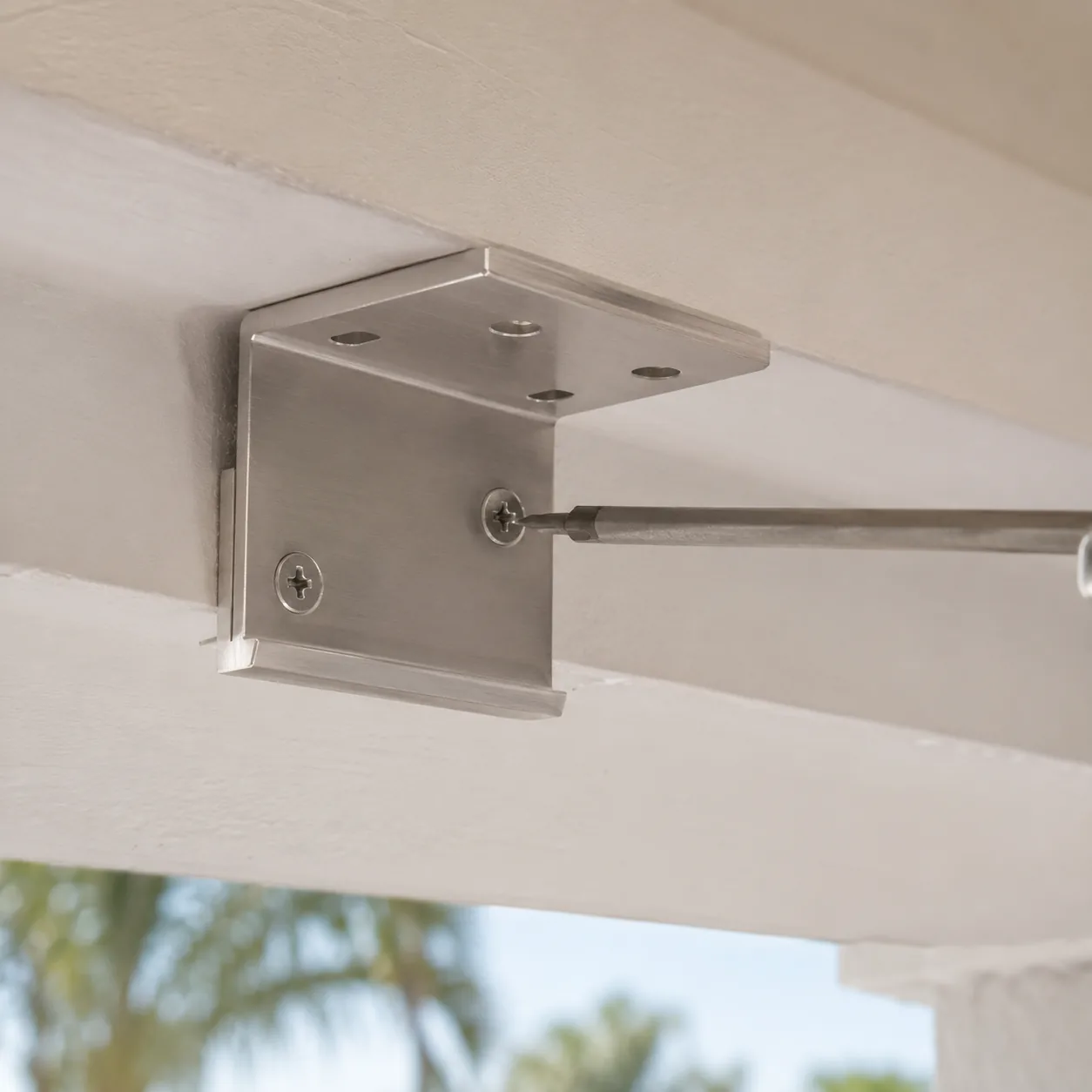 Brushed aluminum head-rail bracket being mounted to a ceiling joist during exterior shade installation